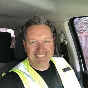 Paco the Plumber, 
    wearing a blue work shirt and cap, smiling and holding a wrench while standing in a bright residential kitchen near a water heater; friendly, professional tone
